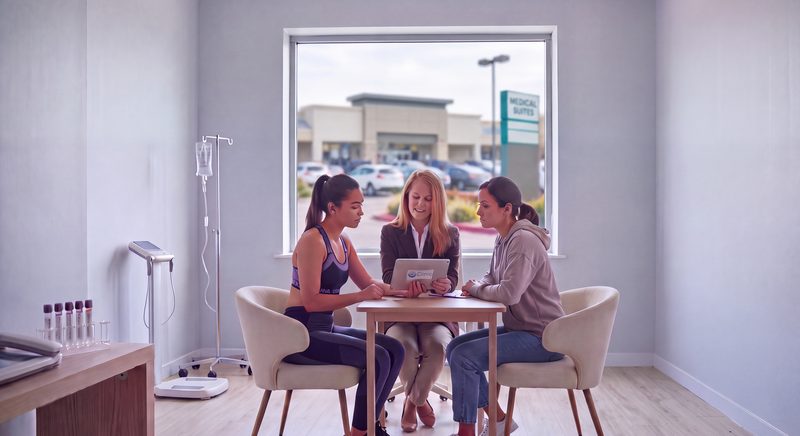 A clinician going over a plan on a tablet with two members at a table in the Paradigm Wellness clinic